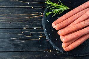 Juicy sausages for barbecue lie on a stone chopping board with rosemary and spices, pepper and coarse salt photo