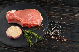 Top view of one pieces raw pork chop steaks with on a black stone cutting board. photo