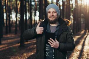 Portrait of adult man walking in the pine forest with digital tablet. photo