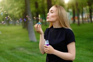 Young beautiful girl inflates soap bubbles in the summer sunny park photo