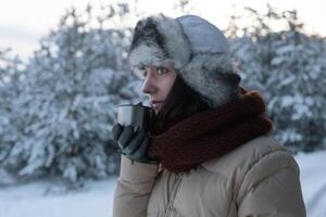 hermosa niña en un Nevado invierno bosque Bebiendo caliente té desde un termo foto