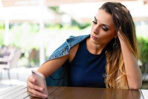 A lonely sad Caucasian girl sits in an open summer cafe with a phone in her hands and is sad alone photo