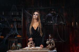 Halloween concept. Witch portrait close up with dreadlocks dressed black hood standing dark room with cage on background photo