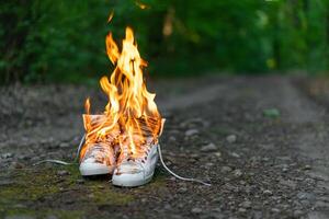 Used white high sneakers burning on a rural road that runs in the forest. photo