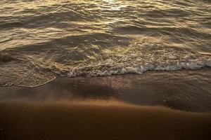 Close up beach wave at sunset. Sun reflecting on serene beach. Soft focus photo