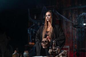 Halloween concept. Witch portrait close up with dreadlocks dressed black hood standing dark room with cage on background photo