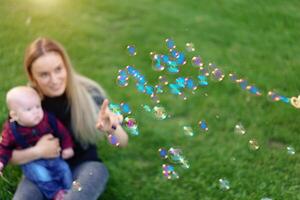 Unfocused unrecognizable mother inflates soap bubbles with her little son in a park on a sunny summer day. focus on the bubbles photo