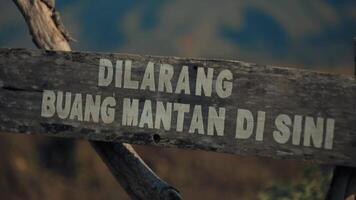 Rustic wooden sign with Indonesian text against a blurred natural background. video