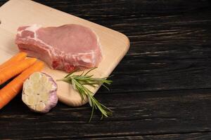 Top view of one pieces raw pork chop steaks with cherry tomatoes rosemary and garlic on a cutting board. photo