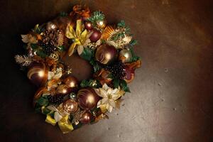 Christmas wreath on brown background with copyspace. Wreath decorated with balls and bows of gold and brown, with green leaves photo