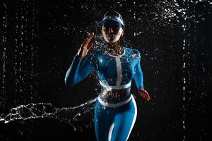 Beautiful young girl in ultramarine blue bird color sportswear runing in aqua studio. Drops of water spread about her fitness body on the background of water splashes. photo