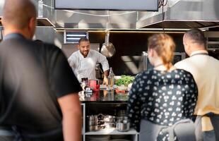 In focus is the chef who conducts a master class in cooking. In the foreground are blurred images of people from the back watching the process photo