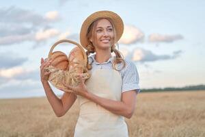 Female farmer standing wheat agricultural field Woman baker holding wicker basket bread product photo