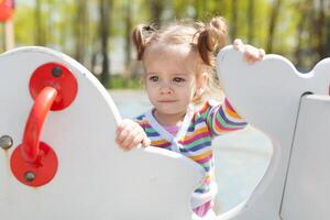 a little girl with two tails is dressed in a striped colorful jacket is playing on the playground photo