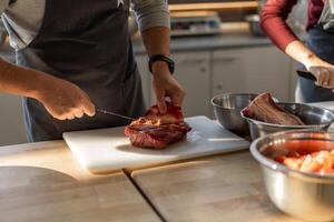 Chef in gray apron cuts meat on a plastic board. Closeup photo of the culinary process