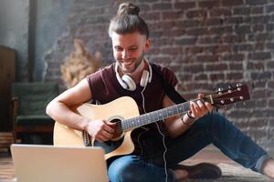 caucásico joven adulto aprendizaje guitarra en línea música clase con distante profesor computadora móvil dispositivo foto