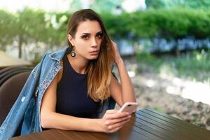 A lonely sad Caucasian girl sits in an open summer cafe with a phone in her hands and is sad alone photo