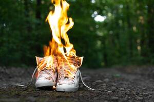 Used white high sneakers burning on a rural road that runs in the forest. photo