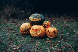 Group of halloween pumpkins with a carved face lying on the ground in a dark mystical forest photo