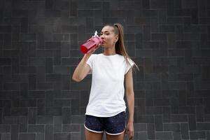 mujer bebida agua rojo botella después Mañana rutina de ejercicio ciudad antecedentes foto