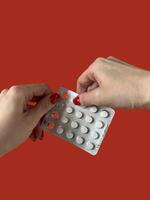 Close-up view of blister pack with pills in female hand isolated on red background photo