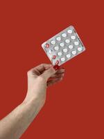 Close-up view of blister pack with pills in female hand isolated on red background photo