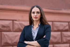 Business woman with long hair dressed black jacket standing outdoor near corporate office building hands folded photo