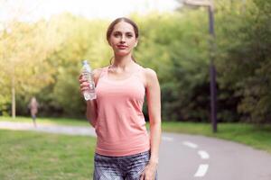 Athletic woman standing running track in summer park drink water after running exercises photo