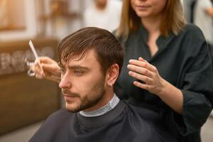 Handsome blue eyed man sitting in barber shop. Hairstylist Hairdresser Woman cutting his hair. Female barber. photo