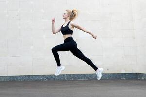 deporte y aptitud concepto joven adulto caucásico hembra atleta saltando alto al aire libre gris cola pared antecedentes foto