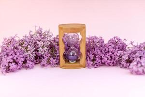 Sand running through the bulbs of an hourglass measuring the passing time in a countdown to a deadline, on a flower lilac spring background with copy space. photo