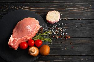 Top view of one pieces raw pork chop steaks with cherry tomatoes Champignon mushrooms on a black stone cutting board. photo