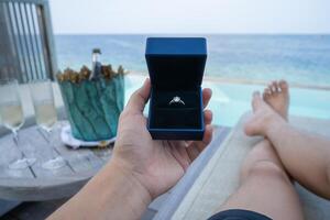 Hand holding a box with engagement ring with ocean view background. photo
