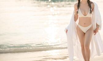 mujer en blanco bikini caminando en el playa durante puesta de sol. foto