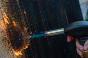 profesional carpintero utilizando antiguo tradicional japonés técnica. ardiente madera tablones con gas quemador foto