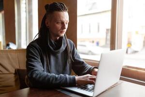 joven empresario con rastas teniendo haciendo su trabajo en café con ordenador portátil. foto