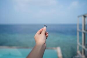 Hand holding engagement ring with ocean view background. photo