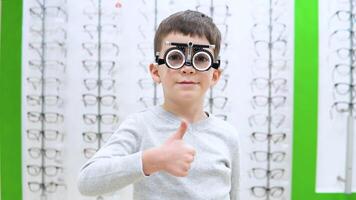 pequeño chico soportes en un antecedentes de un mostrar ventana con marcos para gafas con el dispositivo para selección de contacto lentes video