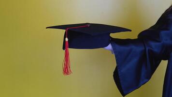 maîtrise chapeau avec une rouge gland sur le main de une Université diplômé. proche en haut vue sur une Jaune Contexte video