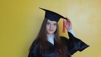 caucásico niña estudiante corrige el sombrero en su cabeza mientras quedarse en frente de cámara con graduarse diploma en su manos. Maestro de educación video