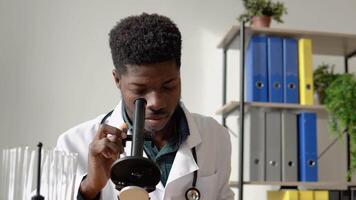 African male doctor working with pathogen samples. Young african american scientist looking through a microscope in a laboratory video