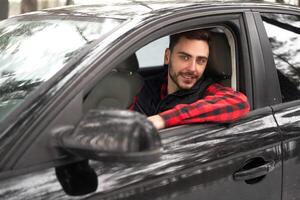 joven atractivo caucásico hombre se sienta a el rueda de su coche soleado invierno día. foto