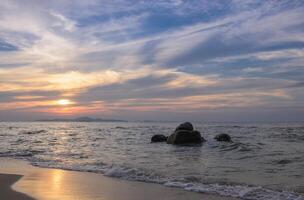 Ocean at sunset with sun reflection on sand and rocks on sea photo