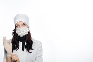 a woman in a white coat and mask is putting a glove on photo