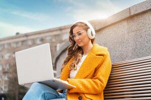 Business Woman Wear Eyeglasses Listen Music Headphone Outdoor Sitting Bench Using Laptop Outdoor photo