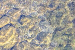 Natural texture in nature with a natural pattern of water waves and stones at the bottom photo