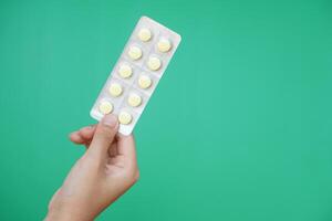 Close up hand hold blister pack of medicine pills. Green background. Concept, pharmacy, medical treatment and health care, use under doctor prescription of illness symptoms. photo