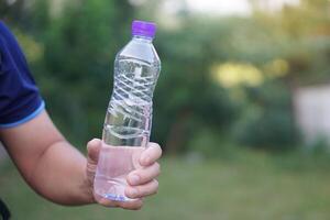 Closeup hand holds drinking water bottle with purple cap. Concept , Drinking water for health, Healthy lifestyle. Quenching thirst, reduce fatigue, refresh body. photo