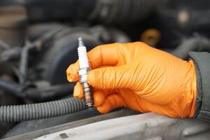 Close up mechanic hands hold old spark plug, spare part of car engine. Concept, machine maintenance, fix, repair, check or diagnose automobile problems by engine specialist. photo