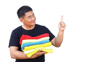 Handsome Asian man hold folded colorful clothes, point finger up. White background. Concept, daily chore, household. Folded clothes for neat and clean. Maintenance and keep garments for sanitary. photo